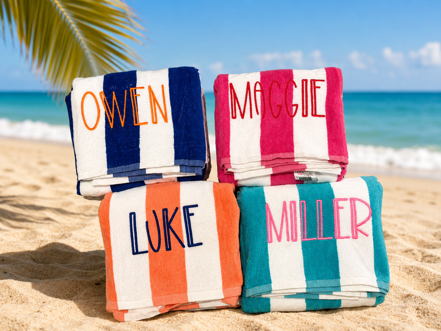 Stacked beach towels with personalized names on a sandy beach with ocean view